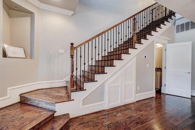 stairway with a high ceiling, hardwood / wood-style flooring, and ornamental molding