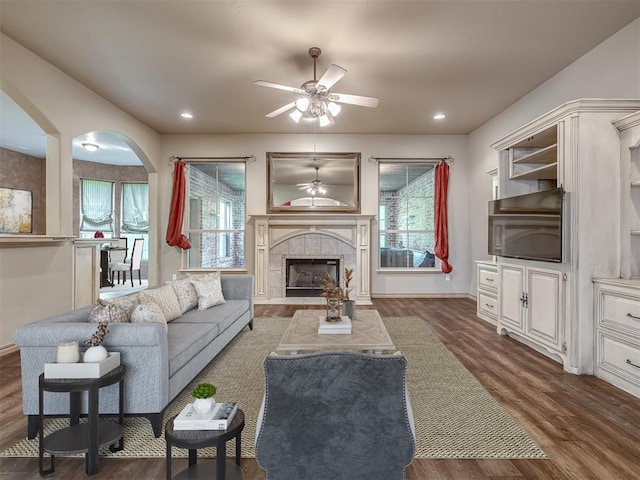 living room with a tile fireplace, ceiling fan, plenty of natural light, and dark hardwood / wood-style floors