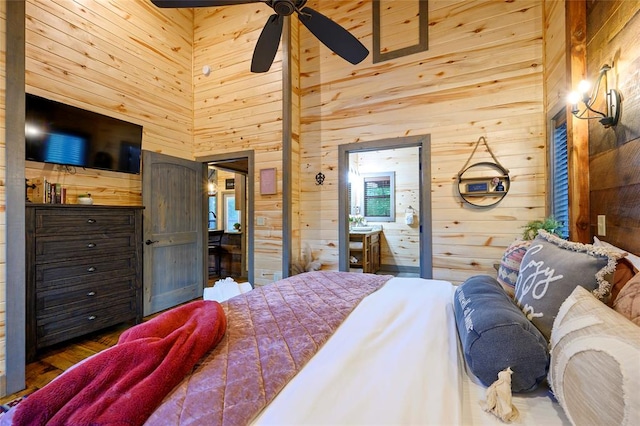 bedroom with wood walls, ensuite bath, hardwood / wood-style flooring, ceiling fan, and a towering ceiling