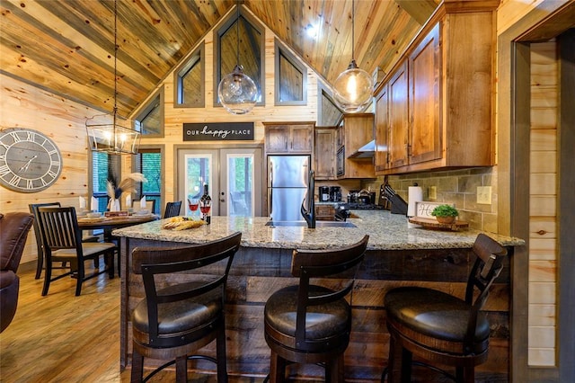 kitchen with hanging light fixtures, wooden ceiling, freestanding refrigerator, and wooden walls