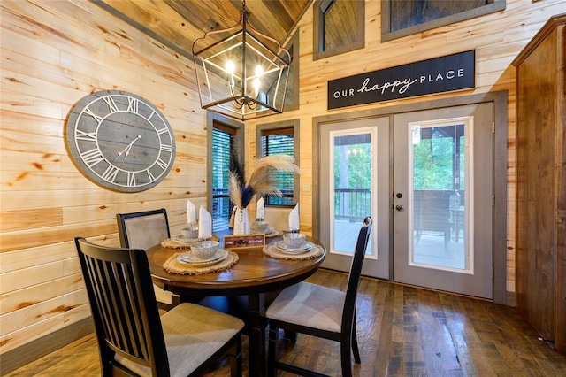 dining room featuring wooden walls, a high ceiling, wood finished floors, french doors, and an inviting chandelier