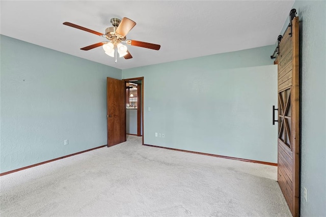 carpeted empty room with a barn door and ceiling fan