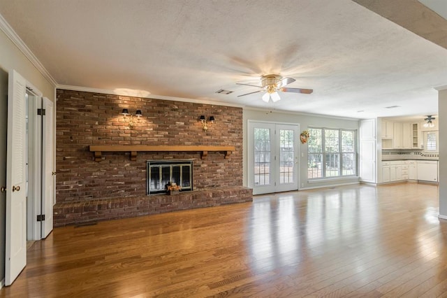 unfurnished living room featuring french doors, crown molding, a brick fireplace, ceiling fan, and wood-type flooring