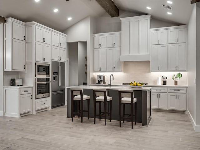 kitchen featuring white cabinetry, a kitchen bar, stainless steel appliances, lofted ceiling with beams, and a center island with sink