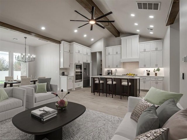 living room with ceiling fan with notable chandelier, sink, vaulted ceiling with beams, and light wood-type flooring