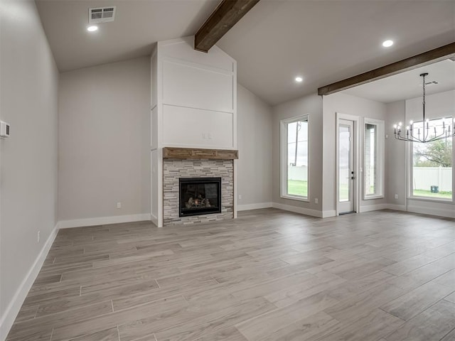 unfurnished living room featuring a notable chandelier, a stone fireplace, lofted ceiling with beams, and light hardwood / wood-style floors