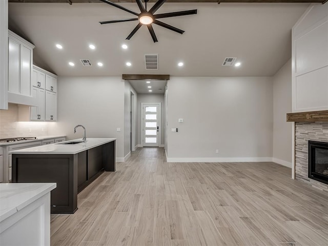 kitchen featuring a stone fireplace, stainless steel gas stovetop, sink, white cabinets, and a kitchen island with sink