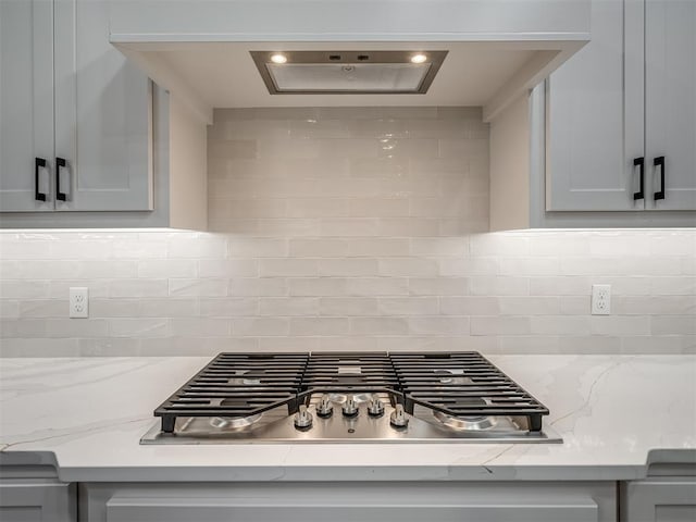 details with stainless steel gas cooktop, gray cabinetry, light stone counters, and decorative backsplash