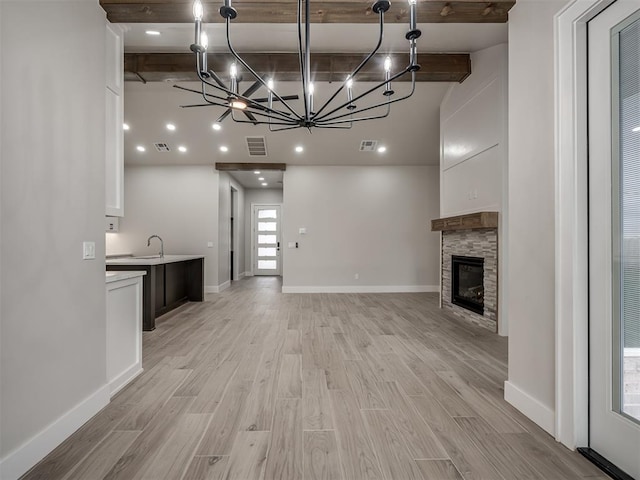 unfurnished living room with beamed ceiling, a stone fireplace, a notable chandelier, and light hardwood / wood-style floors