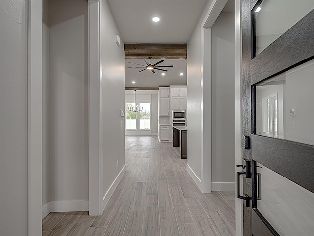 hallway with light hardwood / wood-style floors, a chandelier, and beamed ceiling