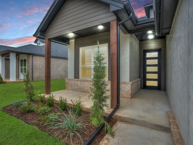 exterior entry at dusk featuring a yard and a patio