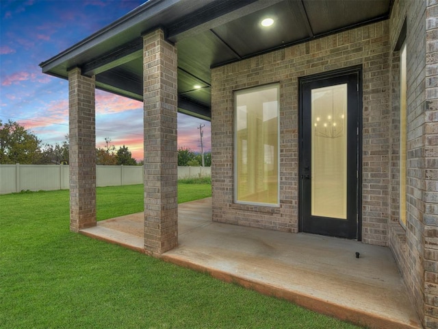 exterior entry at dusk featuring a yard and a patio area