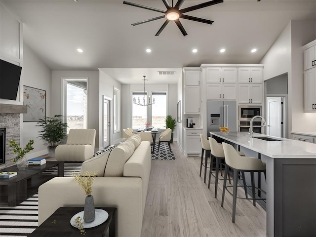 living room featuring sink, light hardwood / wood-style floors, vaulted ceiling, a fireplace, and ceiling fan with notable chandelier