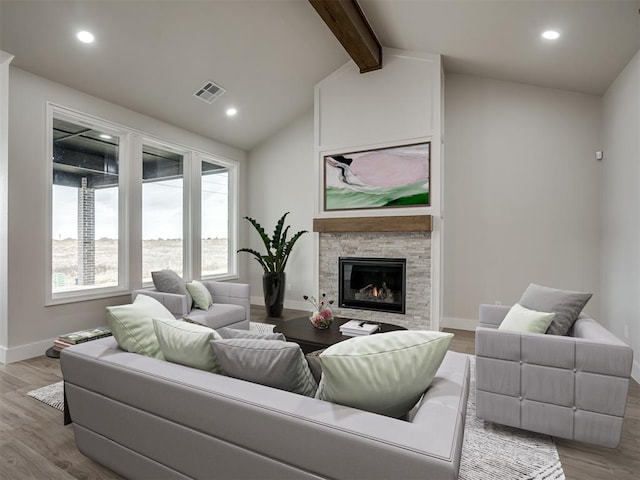 living room with a stone fireplace, vaulted ceiling with beams, and light wood-type flooring