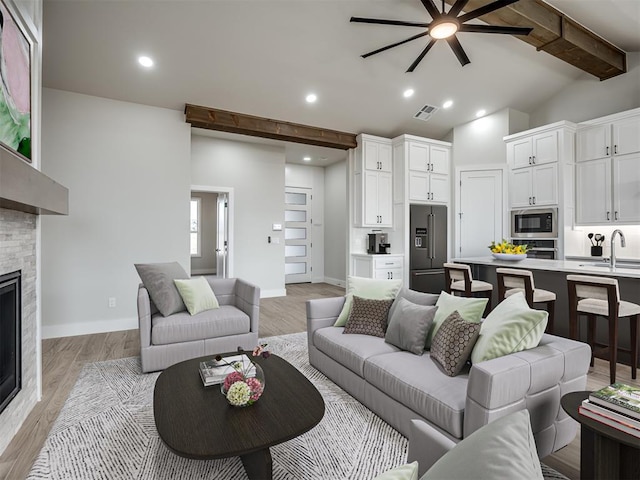 living room featuring sink, a stone fireplace, lofted ceiling with beams, and light hardwood / wood-style floors