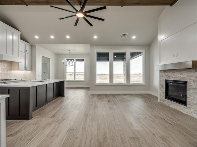 kitchen featuring vaulted ceiling, a fireplace, white cabinets, hanging light fixtures, and gas cooktop