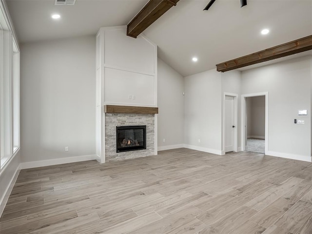 unfurnished living room with lofted ceiling with beams, ceiling fan, a stone fireplace, and light hardwood / wood-style floors