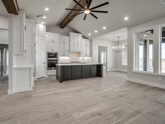 kitchen featuring built in microwave, stainless steel oven, a kitchen island with sink, decorative backsplash, and white cabinets