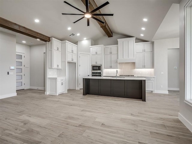 kitchen with built in microwave, sink, an island with sink, and white cabinets