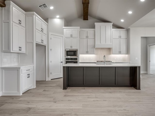 kitchen featuring a kitchen island with sink, vaulted ceiling with beams, white cabinets, built in microwave, and decorative backsplash