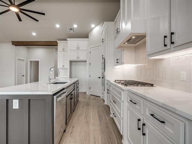 kitchen featuring sink, light stone countertops, an island with sink, and white cabinets