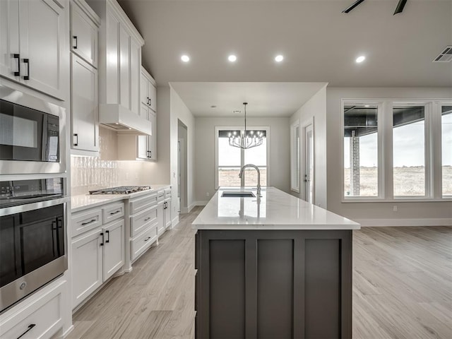 kitchen with sink, backsplash, white cabinets, a center island with sink, and light wood-type flooring