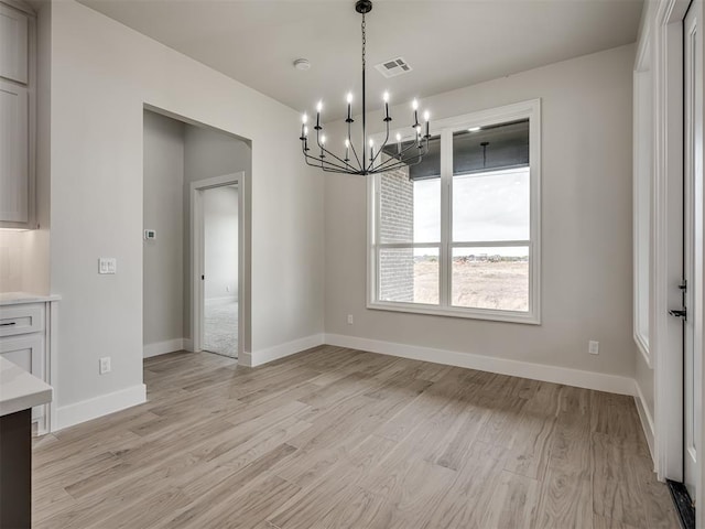 unfurnished dining area with a notable chandelier and light wood-type flooring