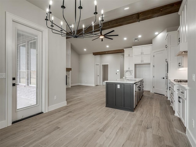 kitchen with a stone fireplace, sink, white cabinetry, light wood-type flooring, and a kitchen island with sink