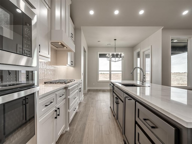 kitchen featuring sink, white cabinetry, stainless steel appliances, light stone counters, and a center island with sink