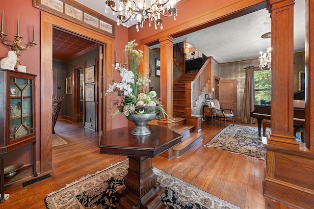 interior space with an inviting chandelier, wood-type flooring, ornamental molding, and decorative columns