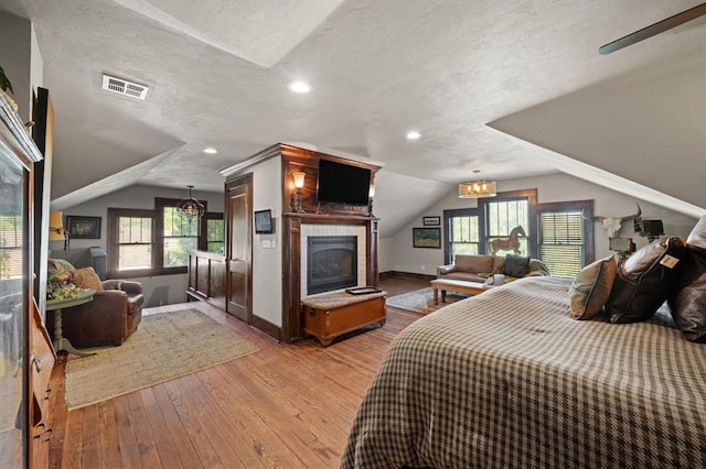 bedroom with a textured ceiling, ceiling fan, light hardwood / wood-style flooring, and vaulted ceiling