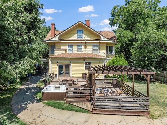 back of property featuring a pergola, a yard, a wooden deck, and a hot tub