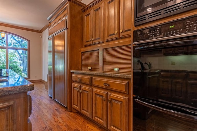 kitchen with stone counters, black double oven, light wood-type flooring, ornamental molding, and tasteful backsplash