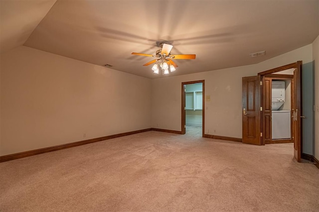 carpeted empty room featuring ceiling fan, lofted ceiling, and stacked washer and clothes dryer