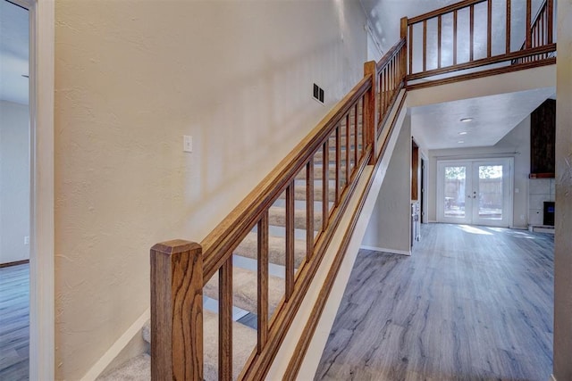 stairs with wood-type flooring, french doors, and a tiled fireplace