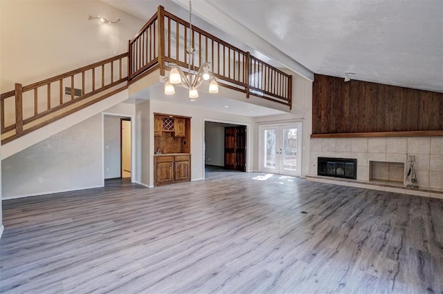 unfurnished living room with a tile fireplace, french doors, high vaulted ceiling, wood-type flooring, and wooden walls