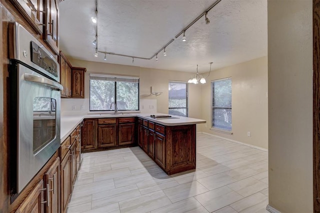 kitchen with track lighting, oven, hanging light fixtures, a notable chandelier, and kitchen peninsula