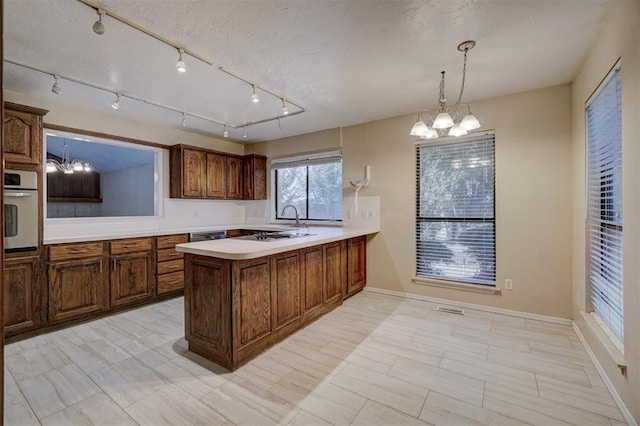 kitchen with stainless steel oven, a notable chandelier, kitchen peninsula, decorative light fixtures, and track lighting