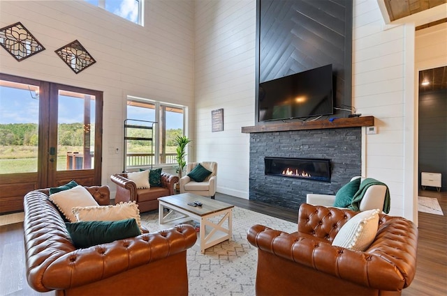 living room with hardwood / wood-style floors, a towering ceiling, a fireplace, and french doors