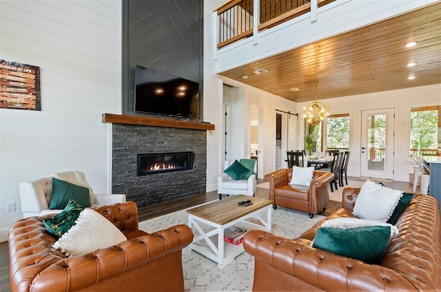 living room with wood ceiling, a notable chandelier, a fireplace, a high ceiling, and light hardwood / wood-style floors