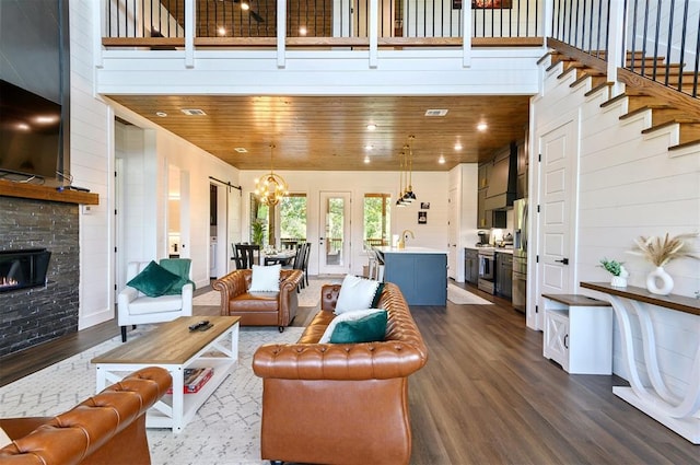 living room with dark hardwood / wood-style flooring, wooden ceiling, a chandelier, a high ceiling, and a stone fireplace