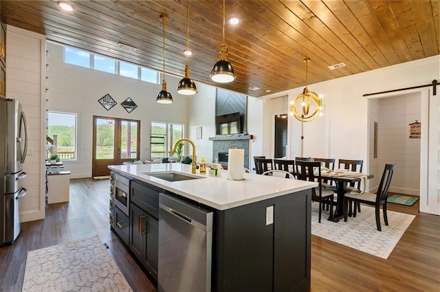 kitchen featuring sink, stainless steel appliances, dark hardwood / wood-style flooring, pendant lighting, and a kitchen island with sink