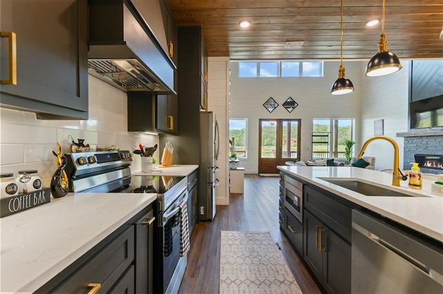 kitchen with sink, wall chimney exhaust hood, dark hardwood / wood-style floors, appliances with stainless steel finishes, and decorative light fixtures