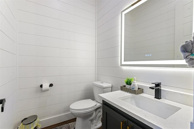 bathroom featuring vanity, toilet, and wooden walls