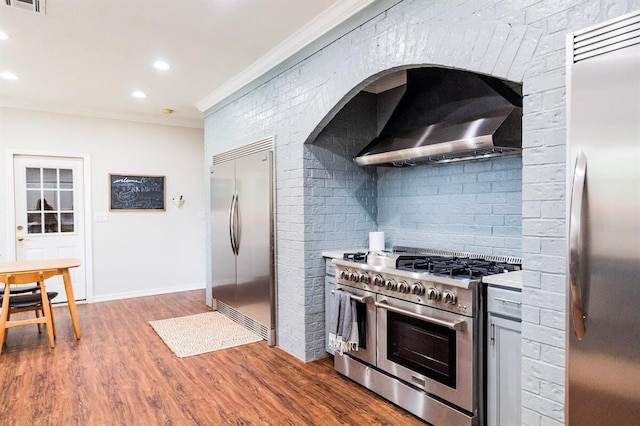 1405 Rosehaven Dr, Altus, OK 73521 - kitchen featuring stainless steel appliances, wall chimney exhaust hood, ornamental molding, light countertops, and wood finished floors