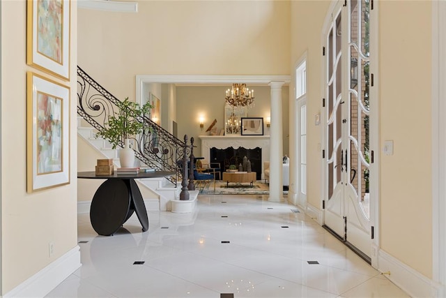 foyer entrance with a fireplace, a high ceiling, decorative columns, and a notable chandelier