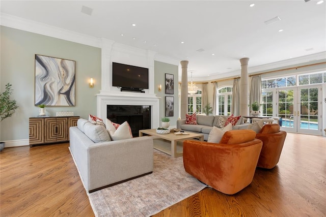 living room featuring french doors, crown molding, a fireplace, light hardwood / wood-style floors, and decorative columns