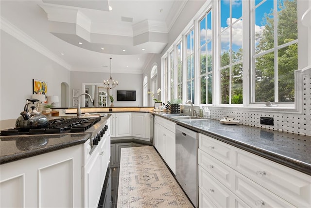 kitchen featuring appliances with stainless steel finishes, dark stone counters, decorative light fixtures, white cabinets, and a chandelier