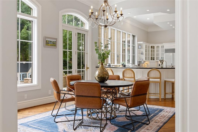 dining space with plenty of natural light, ornamental molding, a notable chandelier, and light wood-type flooring