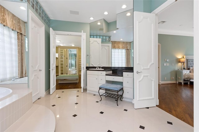 bathroom with wood-type flooring, vanity, a relaxing tiled tub, and ornamental molding